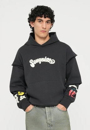 Felpa nera con logo "Songni", grafiche colorate sulle maniche; abbinata a jeans verde chiaro, a vestibilità larga e scarpe da ginnastica bianche.