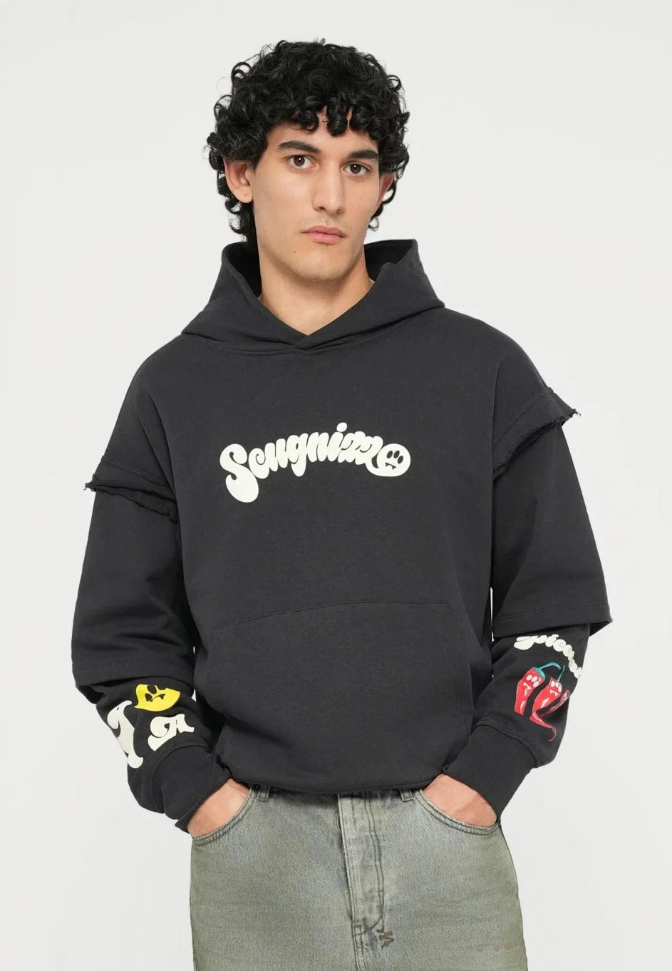 Felpa nera con logo "Songni", grafiche colorate sulle maniche; abbinata a jeans verde chiaro, a vestibilità larga e scarpe da ginnastica bianche.