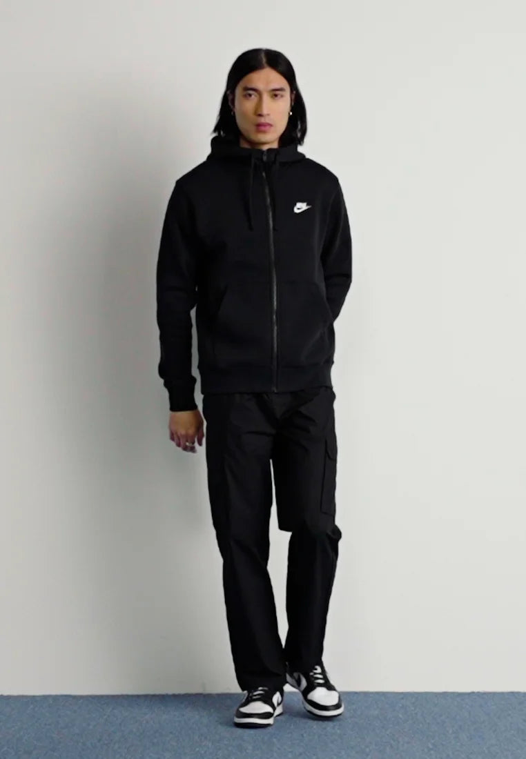Felpa nera con zip e piccolo logo Nike bianco, abbinata a pantaloni cargo neri e sneakers bianche e nere. Tessuto dalla texture liscia.