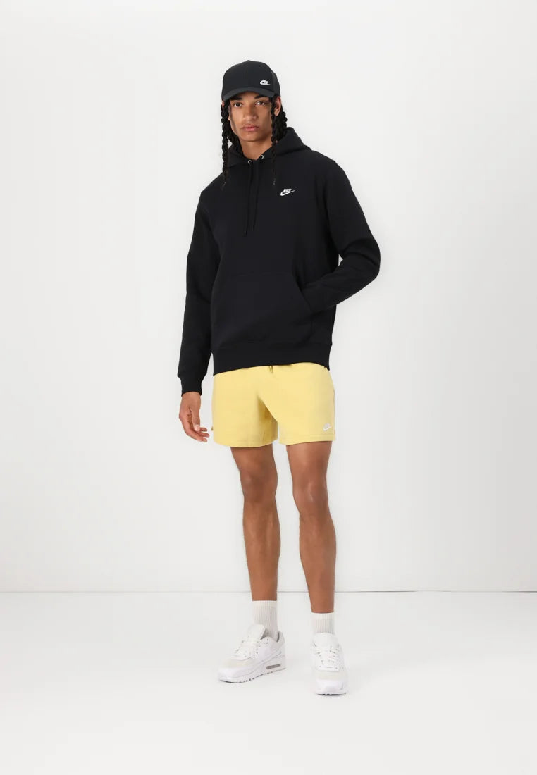 Felpa nera Nike, pantaloni corti gialli e scarpe da ginnastica bianche. Il modello indossa un cappellino nero. L'outfit presenta loghi sulla felpa, sui pantaloni e sulle scarpe.