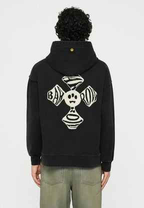Black hoodie with back graphic design featuring a smiling face and circular patterns. Worn with loose-fitting light green jeans and white sneakers.
