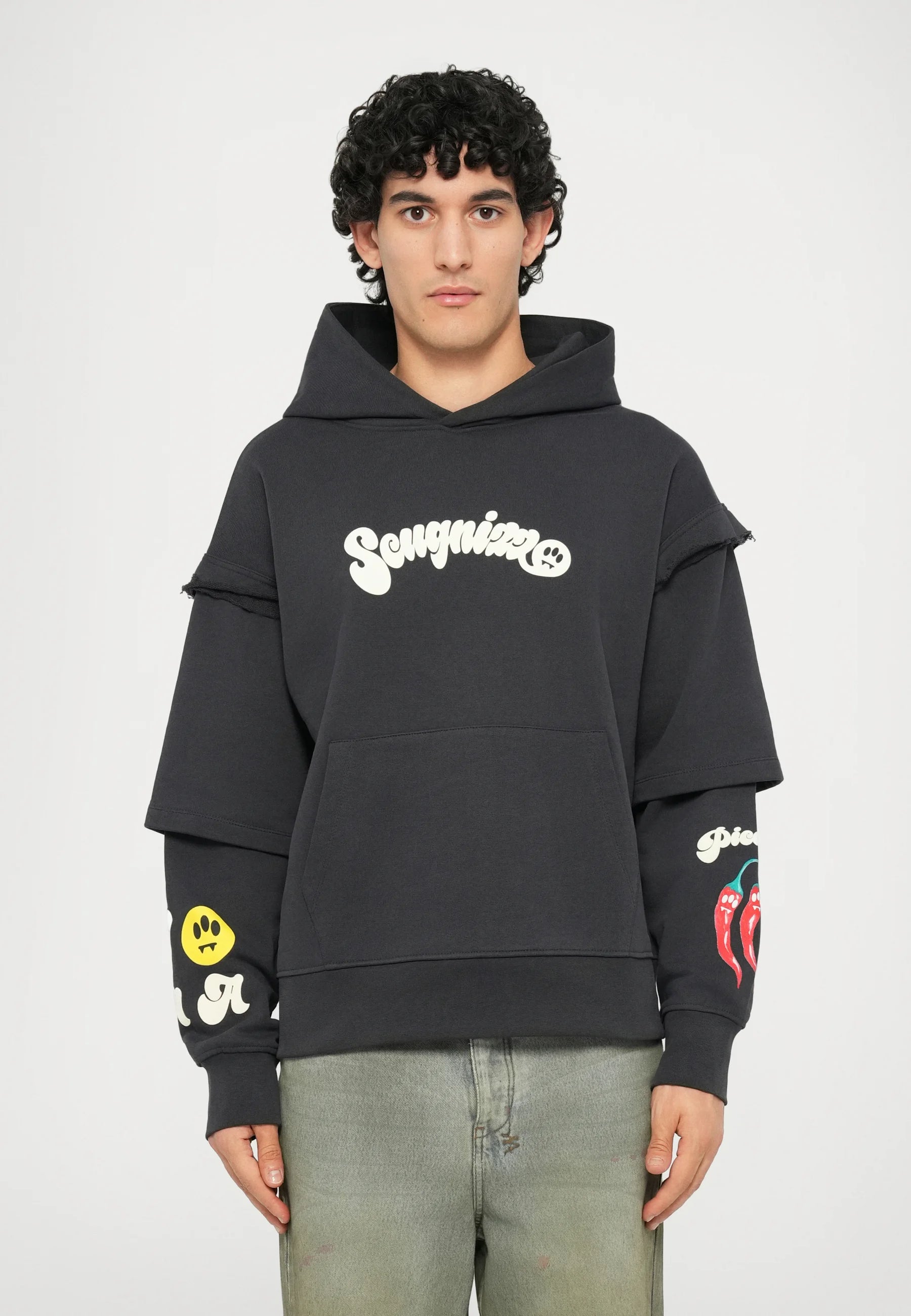 Felpa nera oversize con grafica bianca "Songmin" e smiley giallo sulla manica sinistra; presenta una tasca frontale e bordi sfilacciati.