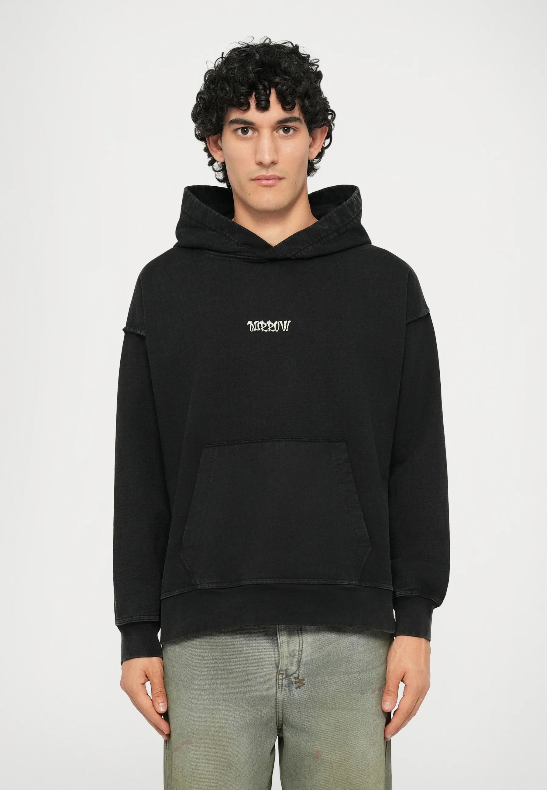 Black hooded sweatshirt with a front pocket, featuring a small white text logo on the chest. Fabric appears soft with a relaxed fit.