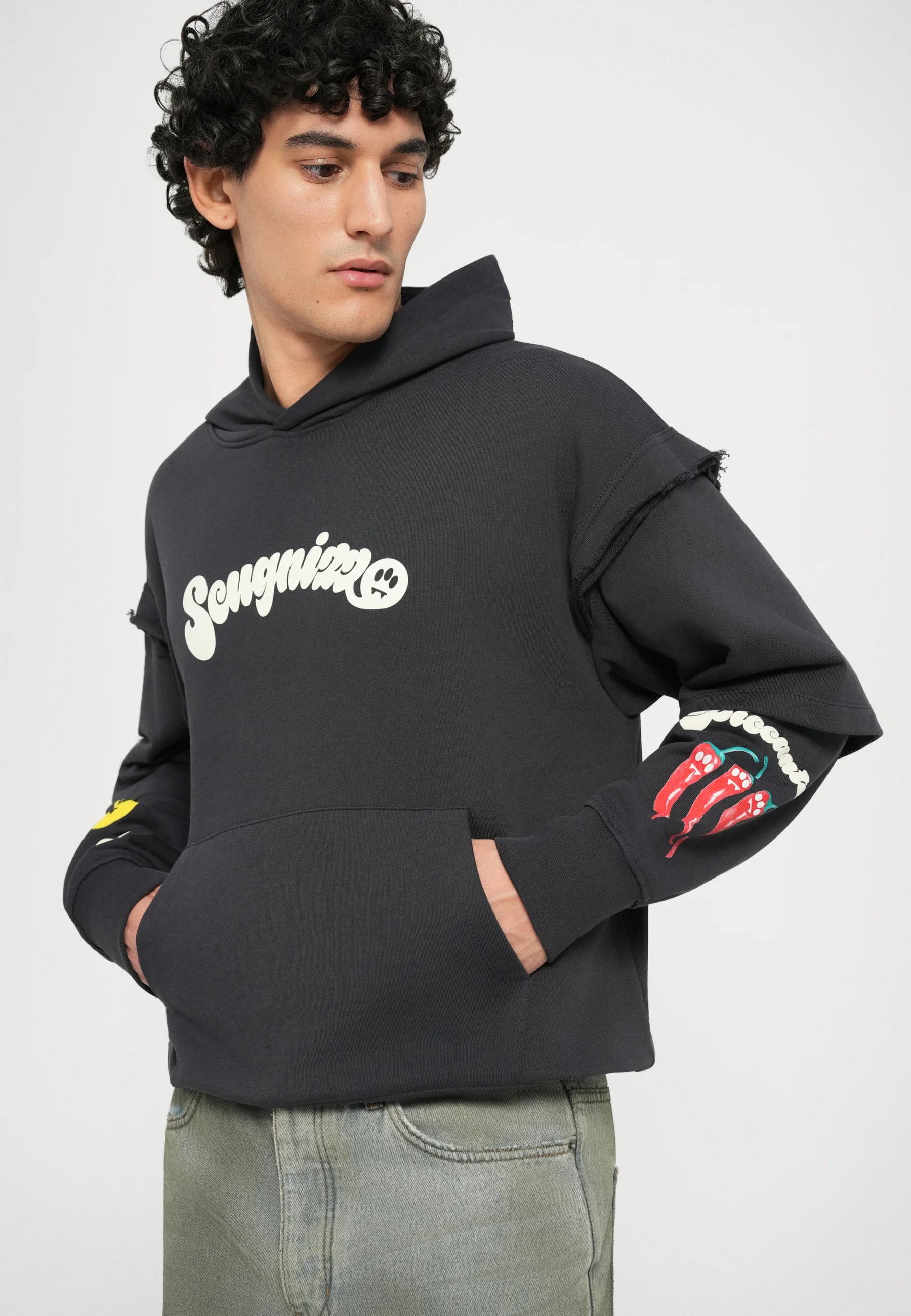 Felpa con cappuccio nera presenta un logo frontale, polsini sfilacciati e dettagli grafici colorati di peperoncini sulla manica destra. Inclusa tasca a marsupio.