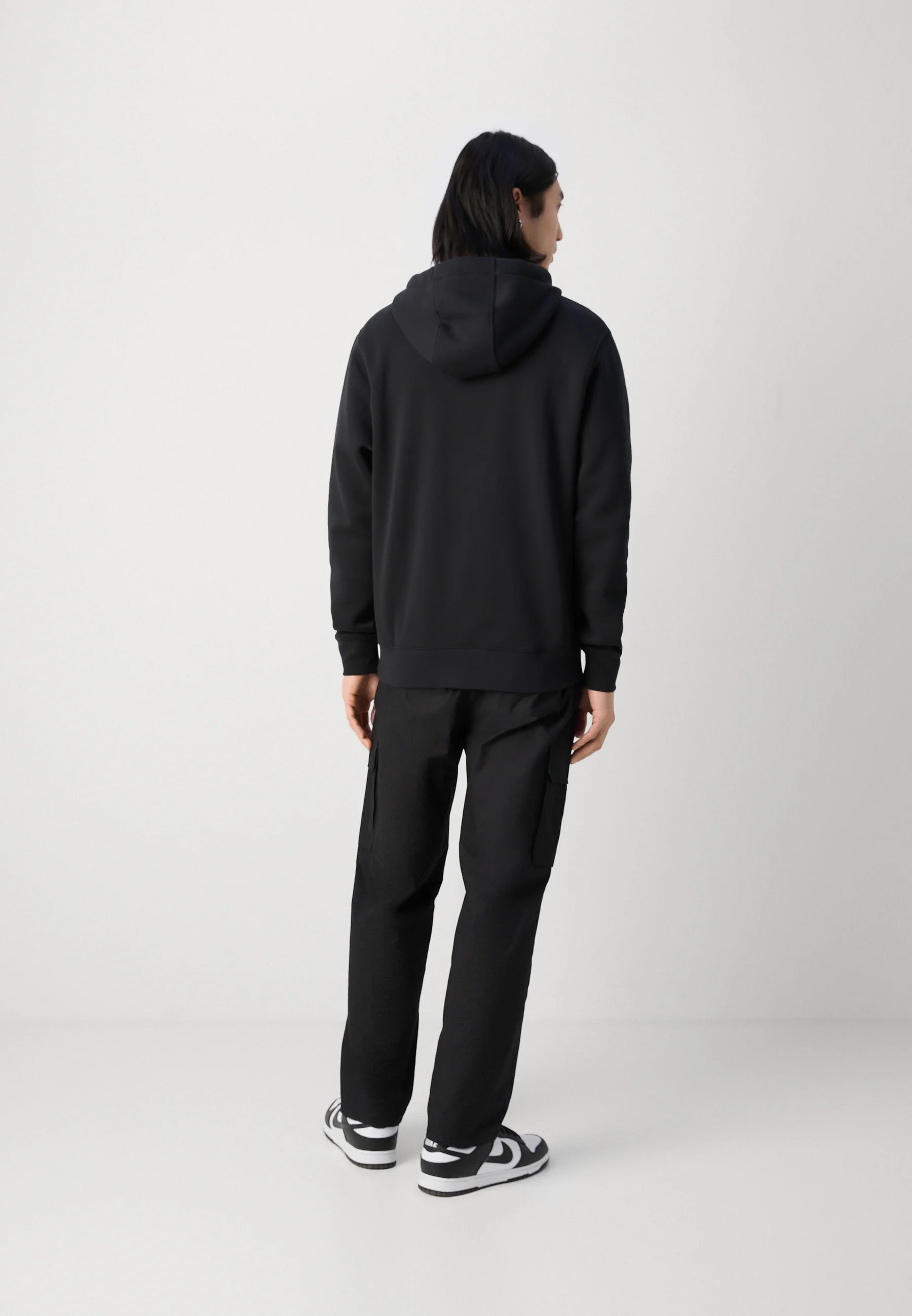 Felpa nera con cappuccio, polsini e orlo a costine, abbinata a pantaloni cargo neri con tasche laterali e sneakers bianche con dettagli neri.