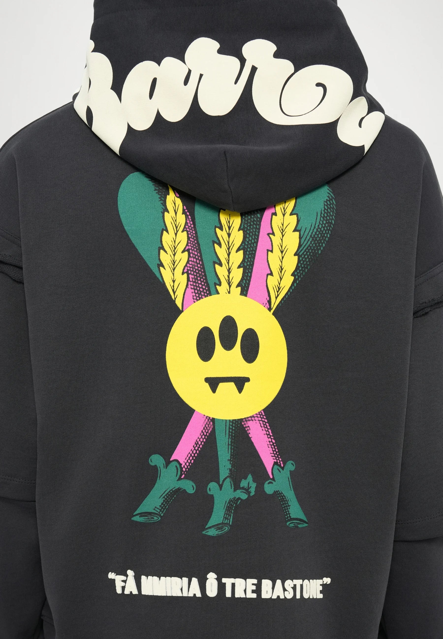 Felpa nera con cappuccio che presenta una grande grafica colorata sul retro: un cerchio giallo con tre occhi, affiancato da piume verdi e accenti rosa.