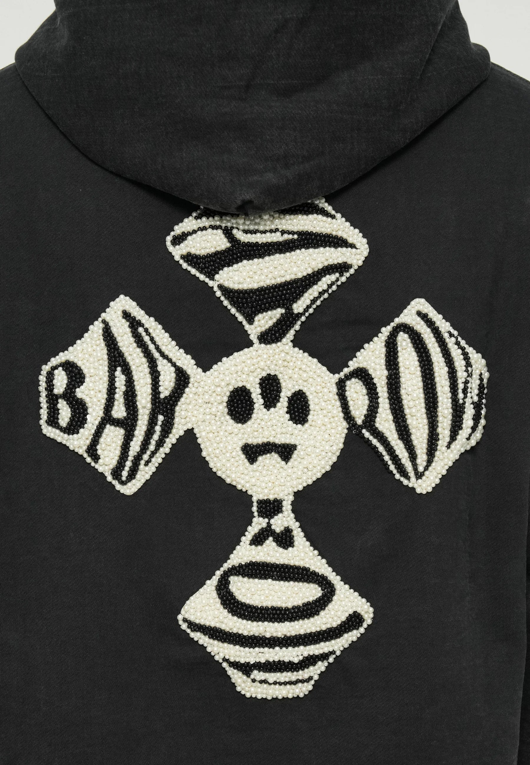 Black hoodie featuring a large textured graphic in white and black beads, depicting a skull and crossbones design with angular shapes.