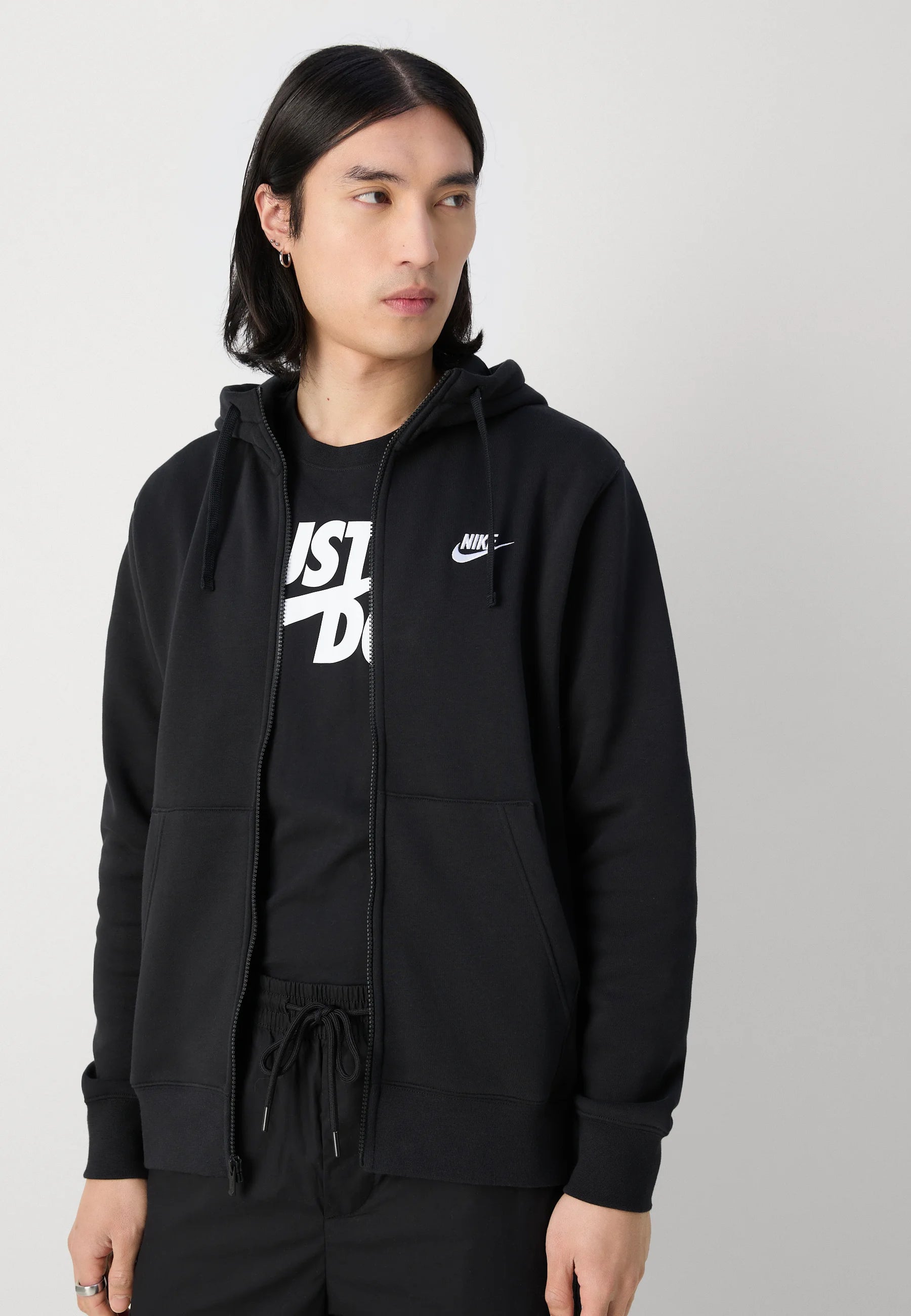 Felpa nera con zip, dotata di tasca frontale, con un logo Nike bianco e la scritta "Just Do It" sulla maglietta sottostante. Texture liscia.